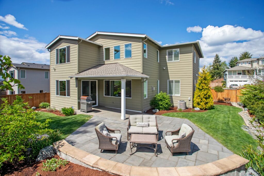 Backyard flagstone patio with outdoor seating, lawn, and planting beds behind a house