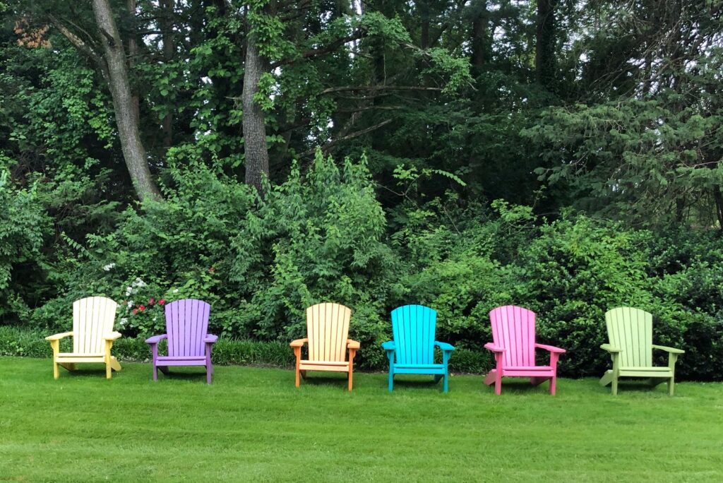 A row of colorful Adirondack chairs on a lawn in front of trees