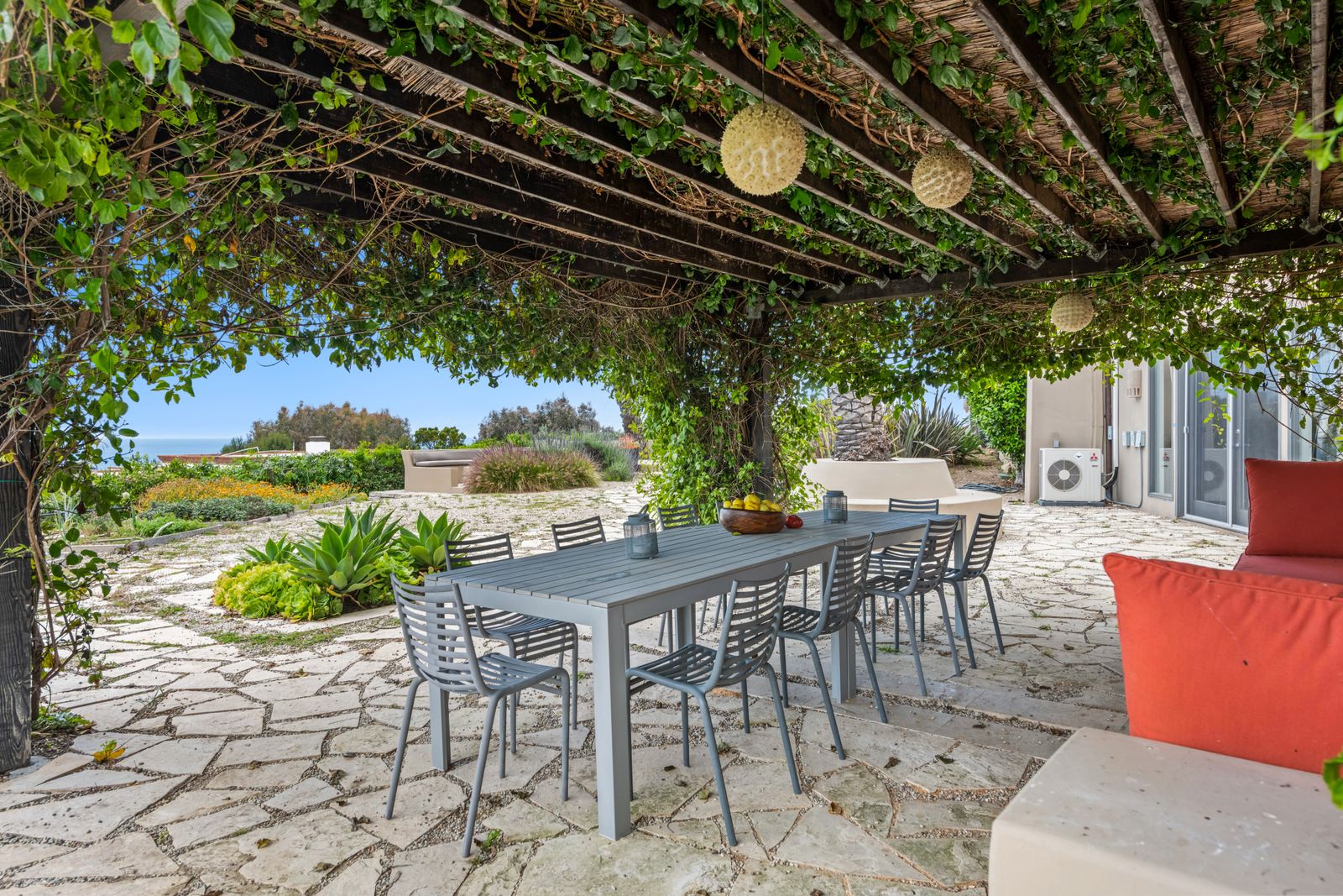 An outdoor dining table and chairs on a stone patio under a vine-covered pergola