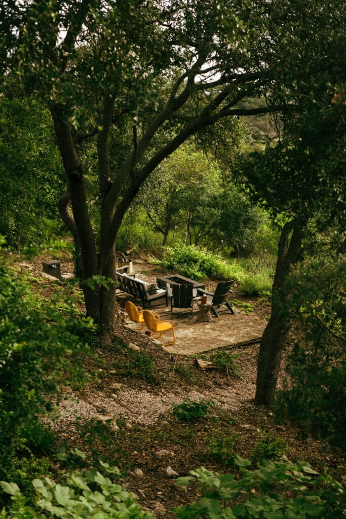 A fire pit seating area on a flagstone clearing among trees, with chairs around the fire