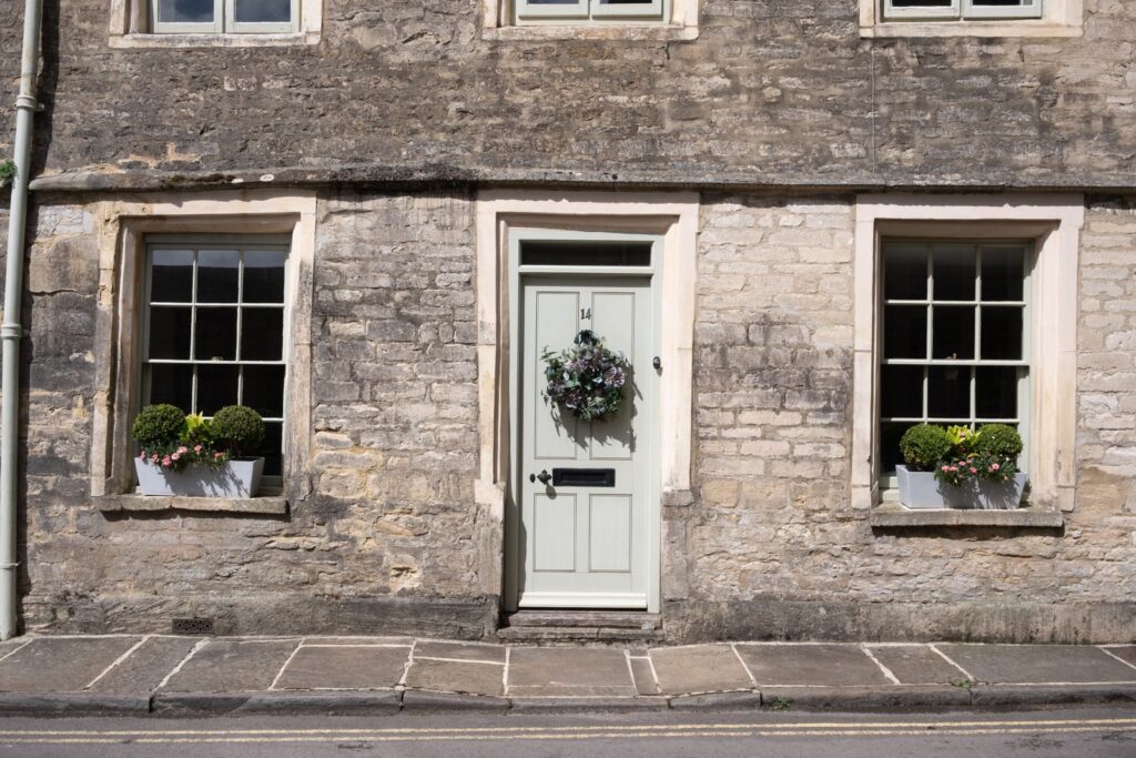 Pale green front door with a wreath, flanked by window planters on a stone house