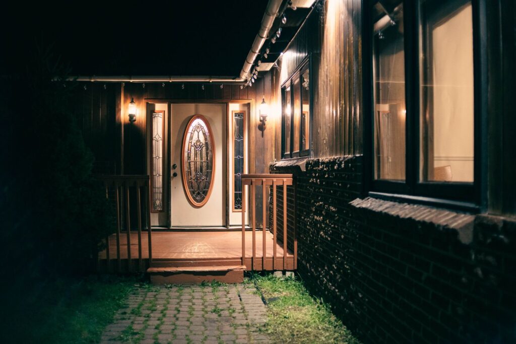 Front entry lit by wall lanterns at night above a brick path