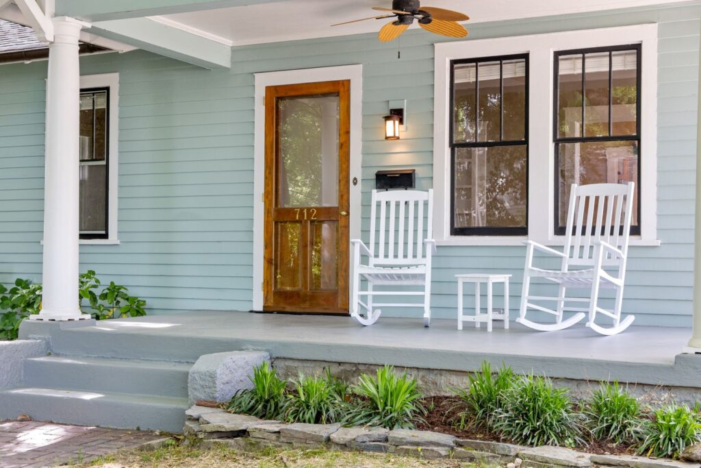 Front porch with white rocking chairs, a wooden door, and low plantings along the steps