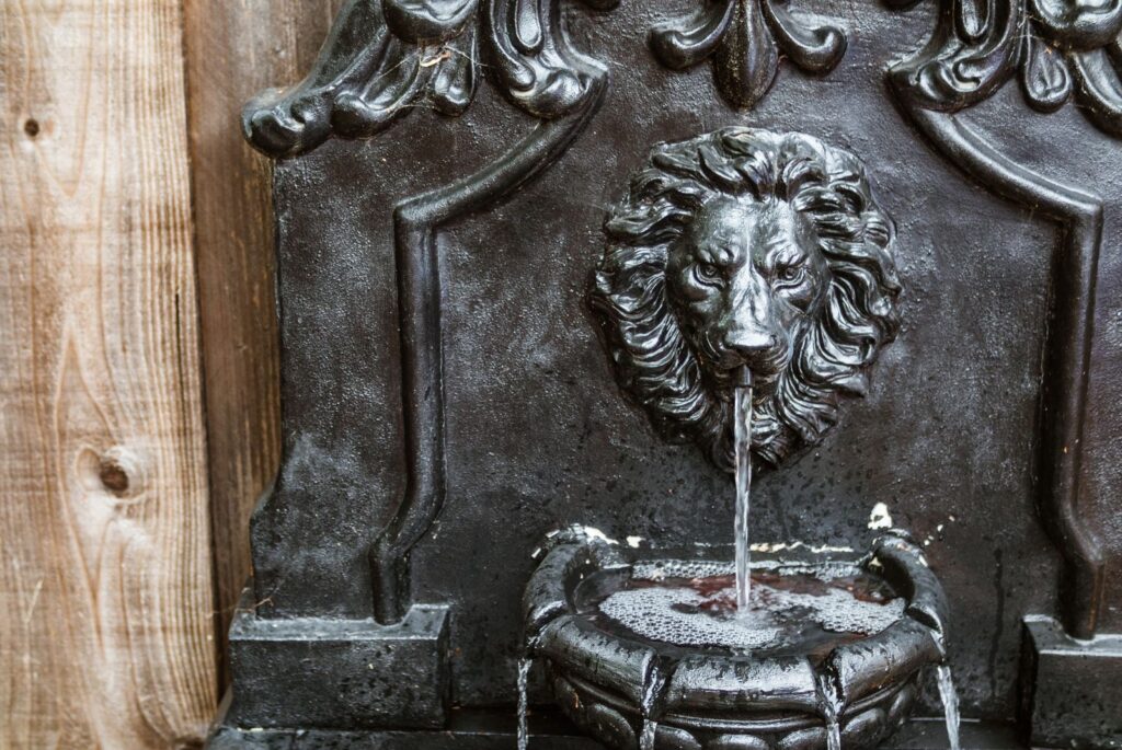 Cast metal lion head wall fountain pouring into a small basin