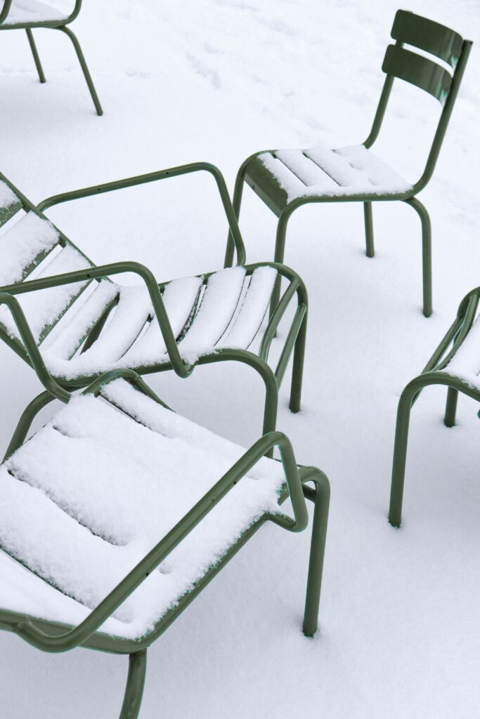 Green metal patio chairs left outside and covered in snow