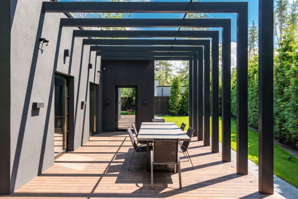A long dining table under a modern dark pergola on a wooden deck