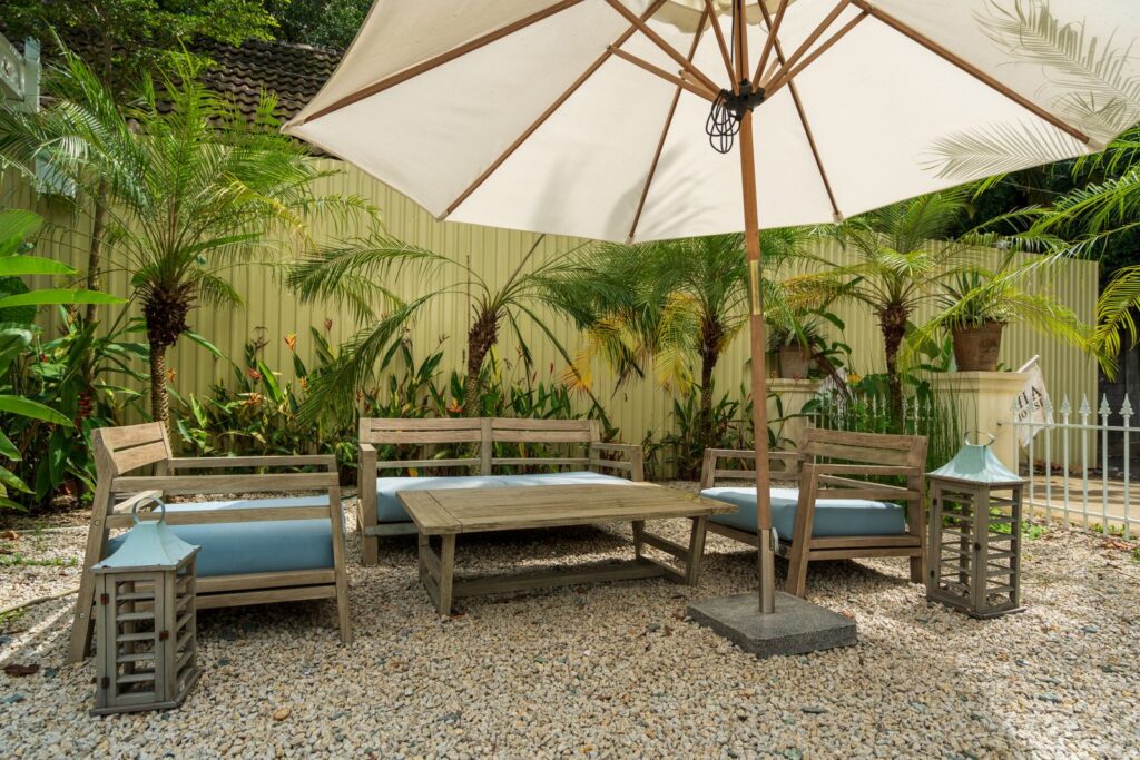 Teak seating set on gravel under a large patio umbrella, surrounded by plants