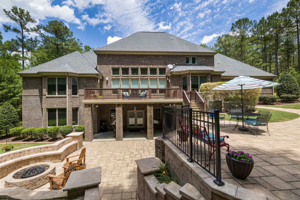 A large backyard paver patio with a fire pit zone, dining table, and umbrella behind a brick house