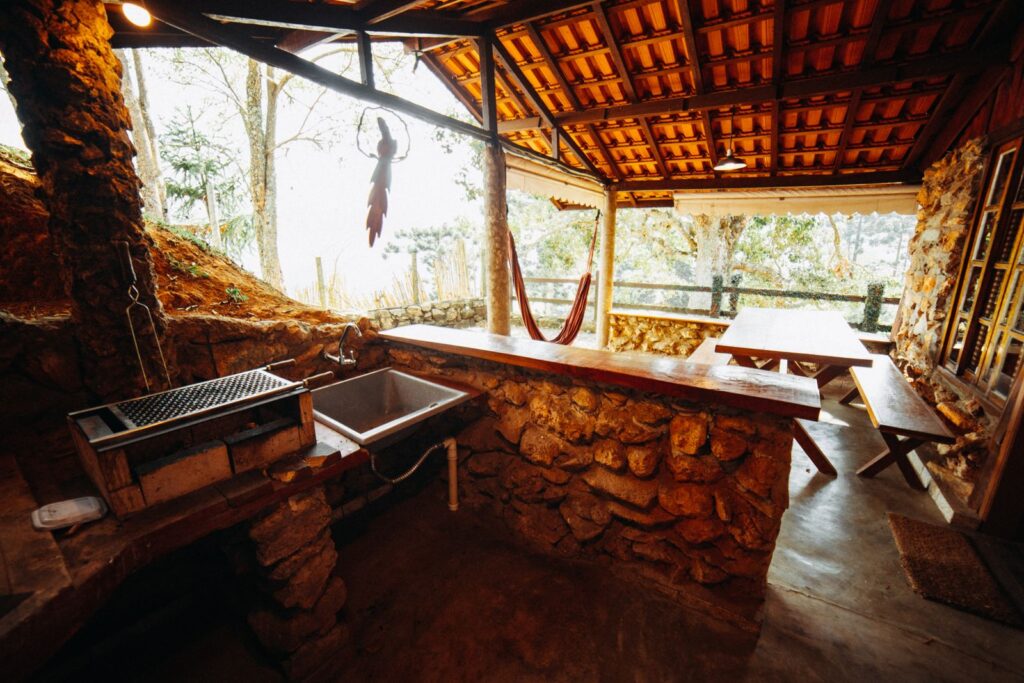 Rustic covered outdoor kitchen with a stone counter, grill, and sink