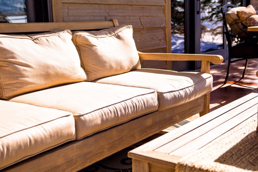 A teak outdoor sofa with tan cushions beside a wooden coffee table