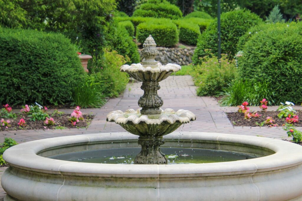 Tiered stone fountain in a basin surrounded by clipped shrubs and flower beds