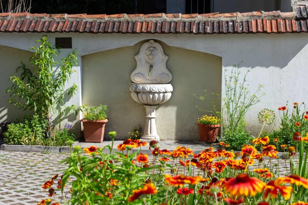 Wall fountain in a courtyard surrounded by potted plants and orange flowers