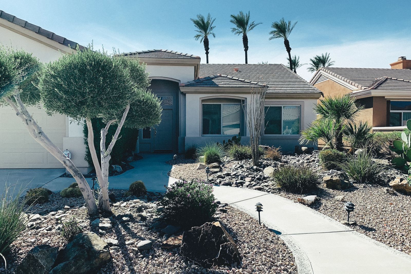 A desert front yard with gravel, boulders, shrubs and a curved walkway