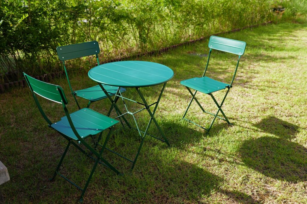 A green folding bistro table and chairs on a lawn