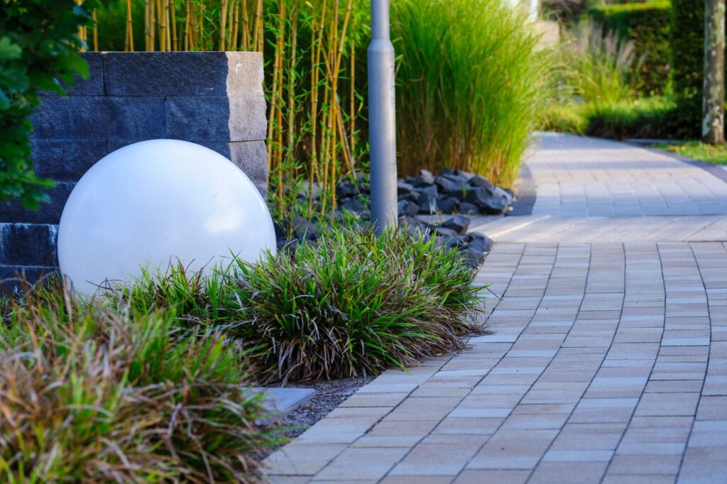 A white garden sphere beside a paver path and ornamental grasses