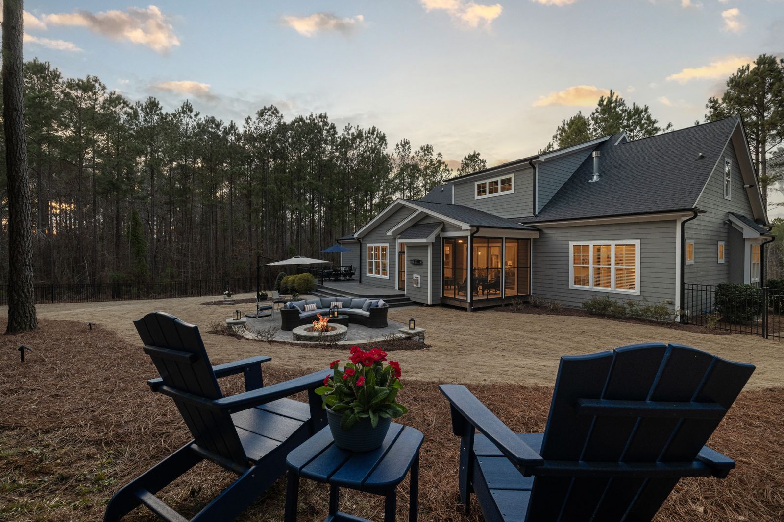 A backyard fire pit area on a gravel pad with Adirondack chairs at dusk
