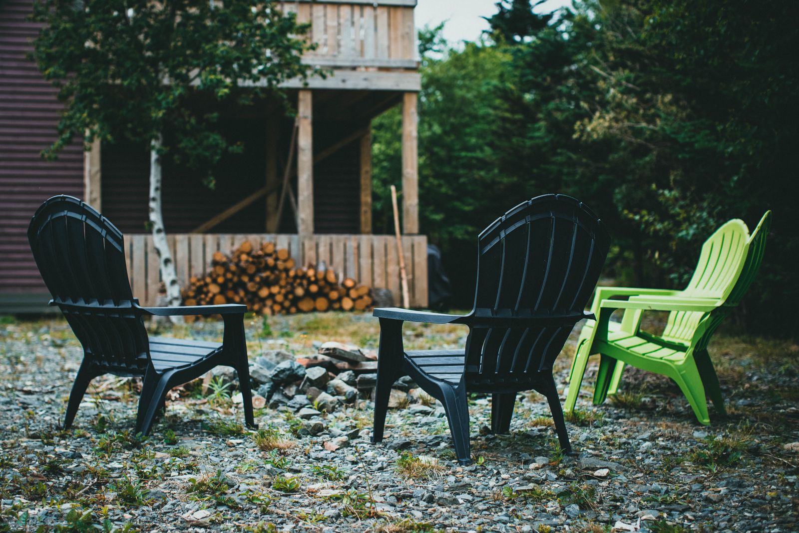 Adirondack chairs around a stone-ringed fire pit on a gravel patio