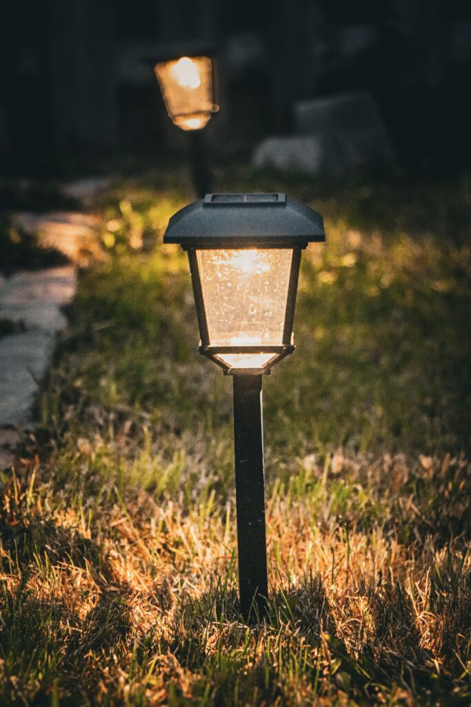 A small hooded path light glowing beside a stepping stone path at dusk