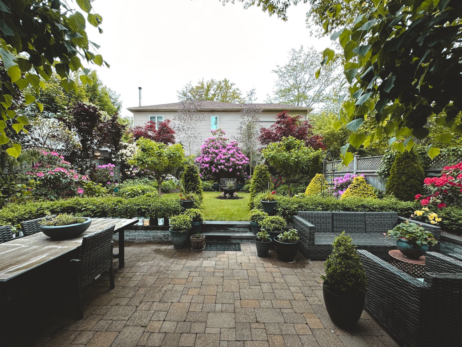 A backyard laid out in zones, with a paved dining patio, steps up to a lawn, and planting around a central urn