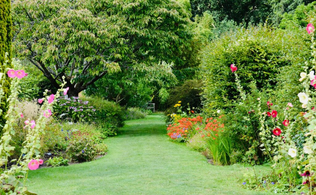Grass path through a layered garden with trees, shrubs, and flowering borders