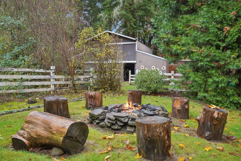 A stone ring fire pit surrounded by log stools in a backyard